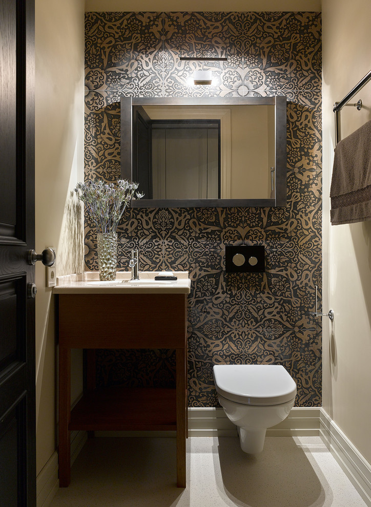 This is an example of a contemporary powder room in Saint Petersburg with a wall-mount toilet, multi-coloured tile, beige walls, an undermount sink, white floor, flat-panel cabinets, medium wood cabinets and white benchtops.