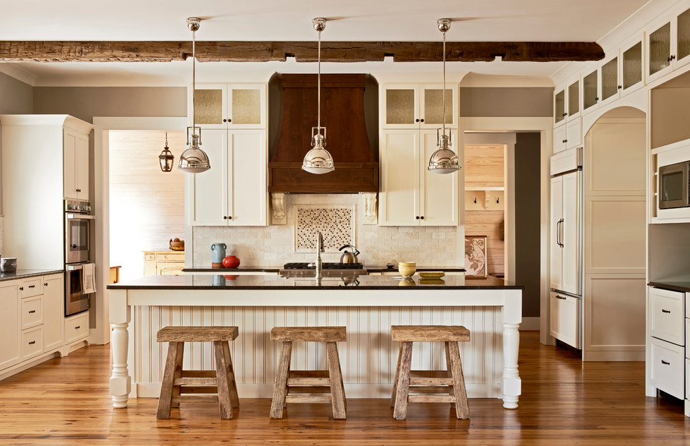 Large transitional l-shaped medium tone wood floor and brown floor open concept kitchen photo in Charlotte with a farmhouse sink, white cabinets, granite countertops, stone tile backsplash, an island, recessed-panel cabinets, multicolored backsplash and paneled appliances