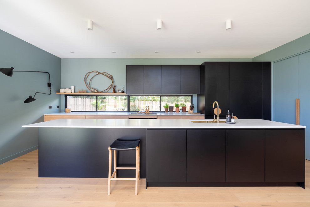 Inspiration for a contemporary galley kitchen in Wollongong with an undermount sink, flat-panel cabinets, black cabinets, panelled appliances, light hardwood floors, with island, beige floor and white benchtop.