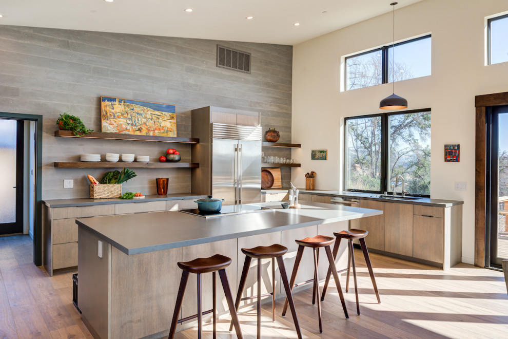 Photo of a mid-sized contemporary u-shaped open plan kitchen in San Francisco with a drop-in sink, flat-panel cabinets, medium wood cabinets, grey splashback, stainless steel appliances, with island and grey benchtop.