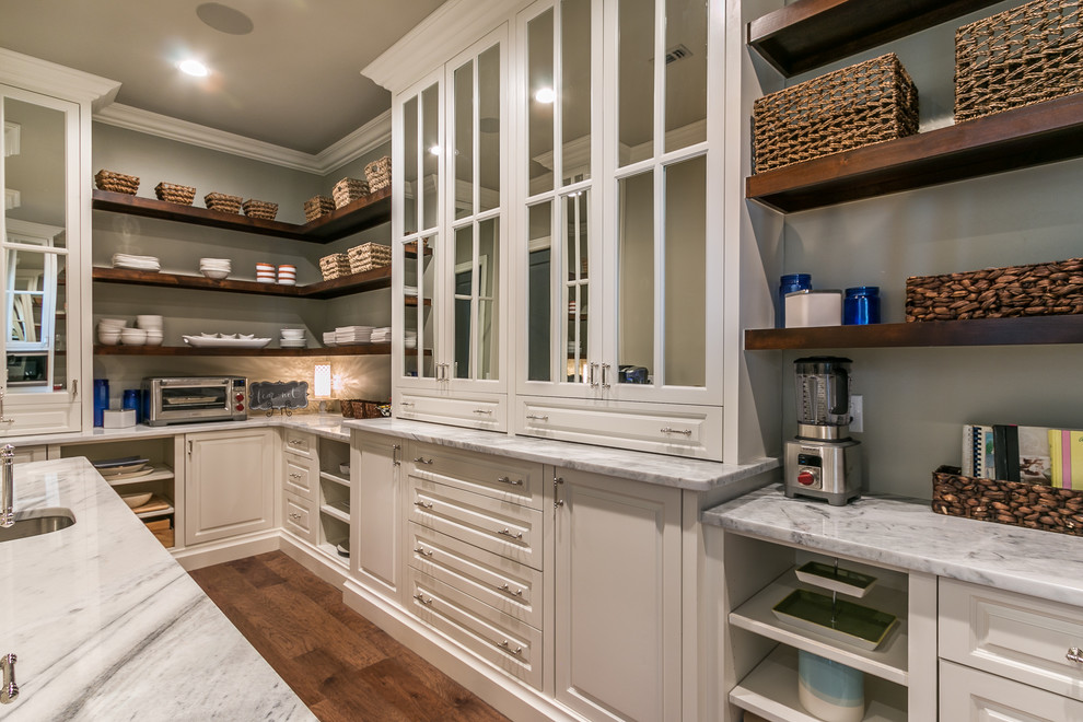 Design ideas for a large transitional u-shaped kitchen pantry in Dallas with a farmhouse sink, raised-panel cabinets, white cabinets, marble benchtops, white splashback, marble splashback, stainless steel appliances, medium hardwood floors, with island and brown floor.