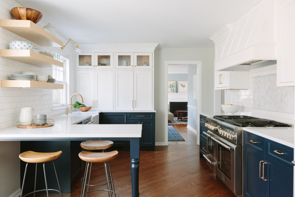 Photo of a transitional u-shaped separate kitchen in Chicago with a farmhouse sink, shaker cabinets, blue cabinets, white splashback, stainless steel appliances, subway tile splashback, medium hardwood floors, a peninsula and white benchtop.