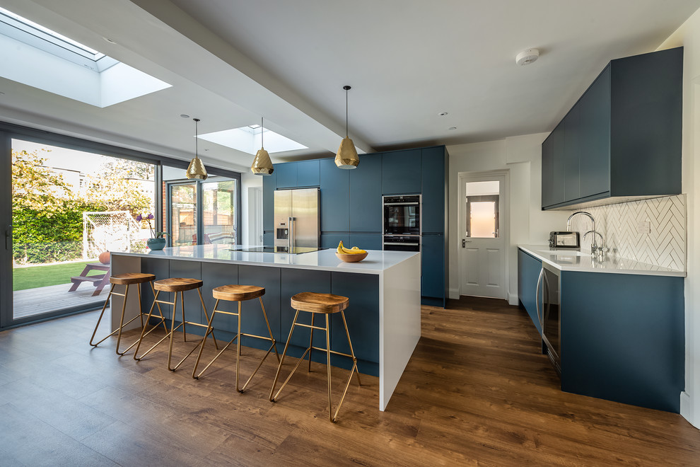 Design ideas for a large modern open plan kitchen in London with a drop-in sink, flat-panel cabinets, blue cabinets, quartzite benchtops, white splashback, subway tile splashback, stainless steel appliances, vinyl floors, with island and white benchtop.