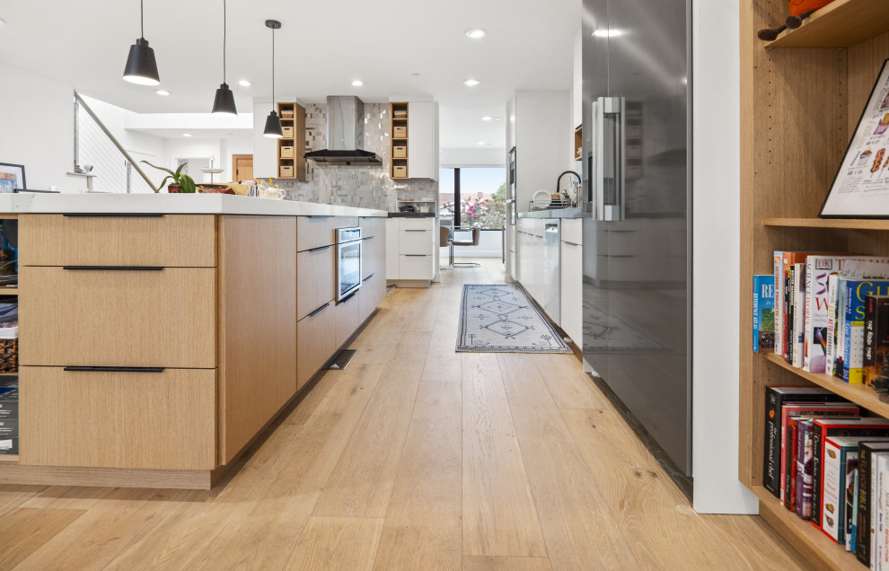 Design ideas for a large modern l-shaped eat-in kitchen in San Francisco with a drop-in sink, flat-panel cabinets, light wood cabinets, grey splashback, glass tile splashback, stainless steel appliances, light hardwood floors, with island, yellow floor and white benchtop.