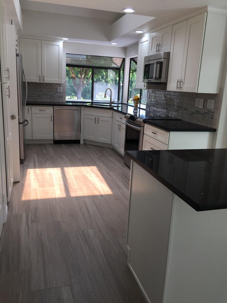 Inspiration for a mid-sized contemporary u-shaped eat-in kitchen in Los Angeles with an undermount sink, shaker cabinets, white cabinets, quartz benchtops, grey splashback, mosaic tile splashback, stainless steel appliances, porcelain floors and with island.