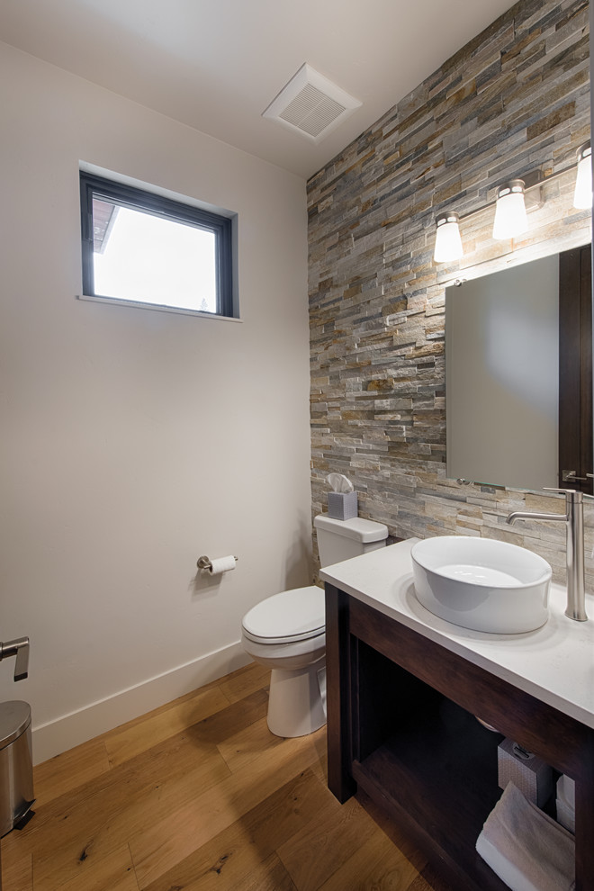 Design ideas for a small contemporary powder room in Boise with furniture-like cabinets, dark wood cabinets, a one-piece toilet, gray tile, stone tile, grey walls, light hardwood floors, a vessel sink, quartzite benchtops and brown floor.
