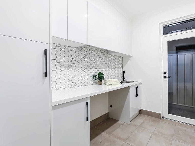 This is an example of a large contemporary single-wall utility room in Adelaide with a drop-in sink, white walls, porcelain floors, a side-by-side washer and dryer, flat-panel cabinets, white cabinets, quartzite benchtops, beige floor and white benchtop.