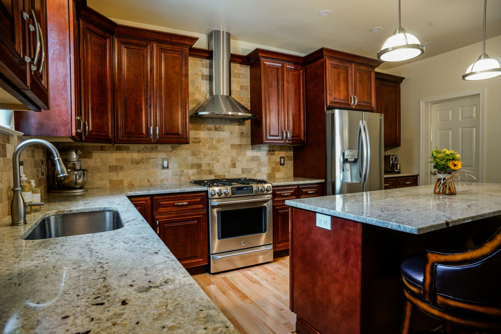 L-shaped eat-in kitchen in Philadelphia with an undermount sink, raised-panel cabinets, red cabinets, granite benchtops, beige splashback, stone tile splashback, light hardwood floors, with island, yellow floor and beige benchtop.