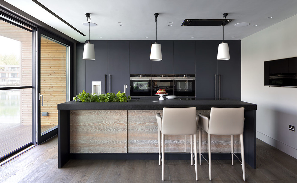 Design ideas for a large contemporary galley kitchen in London with an undermount sink, marble benchtops, with island, flat-panel cabinets, black cabinets, black appliances, dark hardwood floors, brown floor and black benchtop.