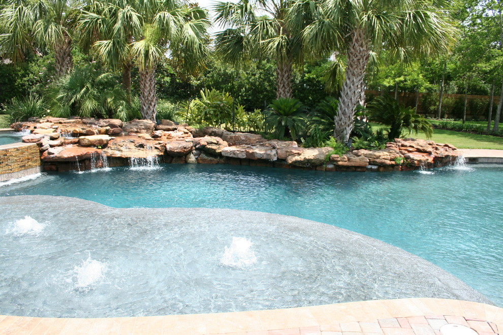 Photo of a large tropical backyard custom-shaped natural pool in Austin with a hot tub and brick pavers.