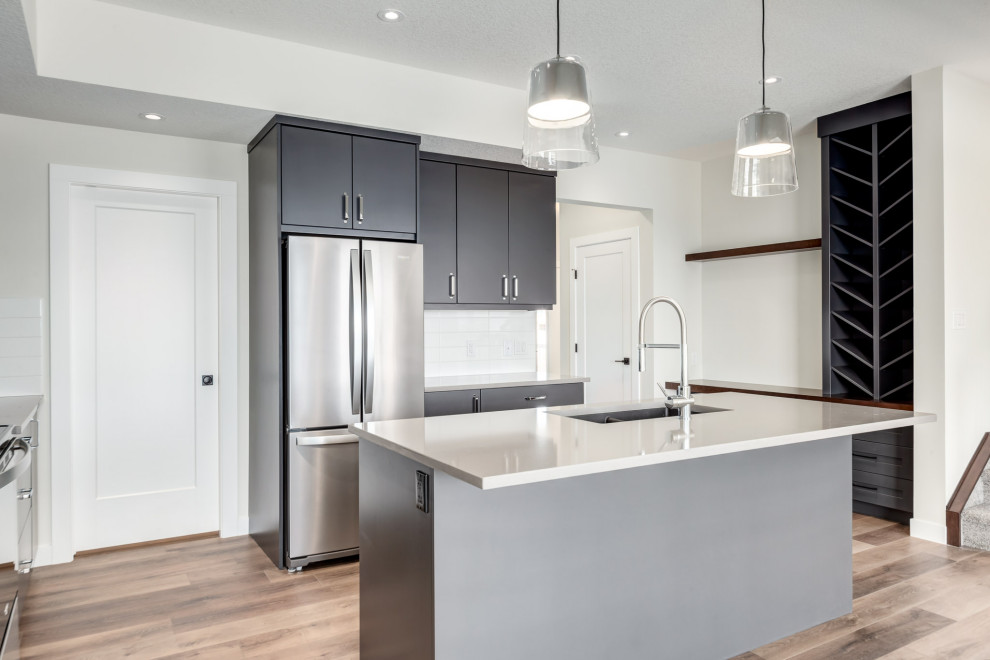 Design ideas for a mid-sized modern l-shaped eat-in kitchen in Calgary with a double-bowl sink, flat-panel cabinets, grey cabinets, quartz benchtops, white splashback, subway tile splashback, stainless steel appliances, vinyl floors, with island, brown floor and grey benchtop.