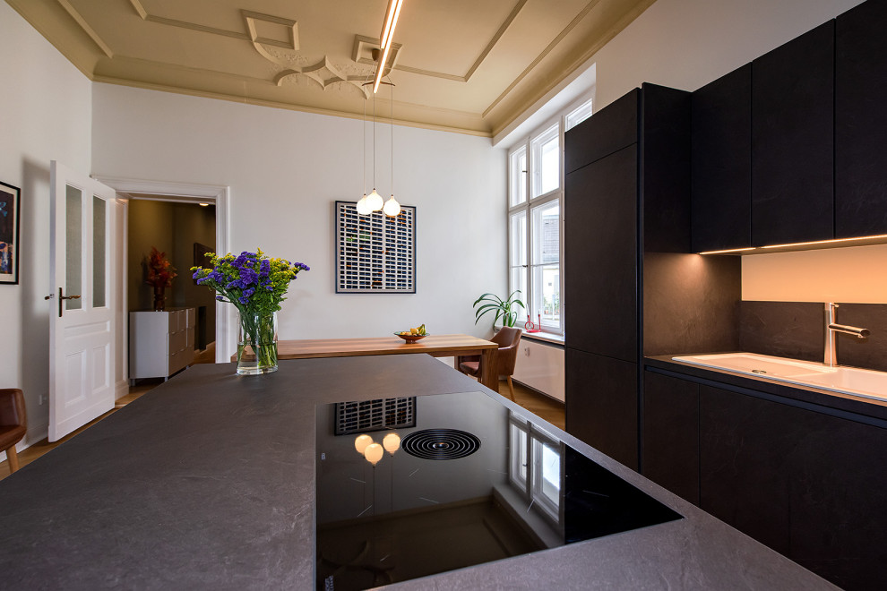Photo of a large eclectic single-wall eat-in kitchen in Berlin with a drop-in sink, grey cabinets, laminate benchtops, black appliances, light hardwood floors, with island, brown floor and grey benchtop.