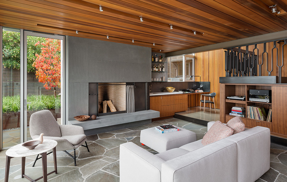 This is an example of a modern open concept living room in Seattle with slate floors, a standard fireplace, a home bar and a concrete fireplace surround.