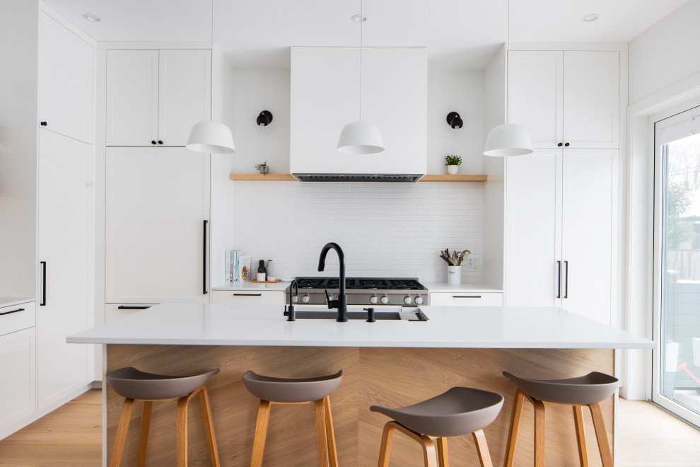Photo of a medium sized scandinavian single-wall open plan kitchen in Vancouver with a built-in sink, flat-panel cabinets, white cabinets, white splashback, stainless steel appliances, an island, beige floors, white worktops, laminate countertops, porcelain splashback and light hardwood flooring.