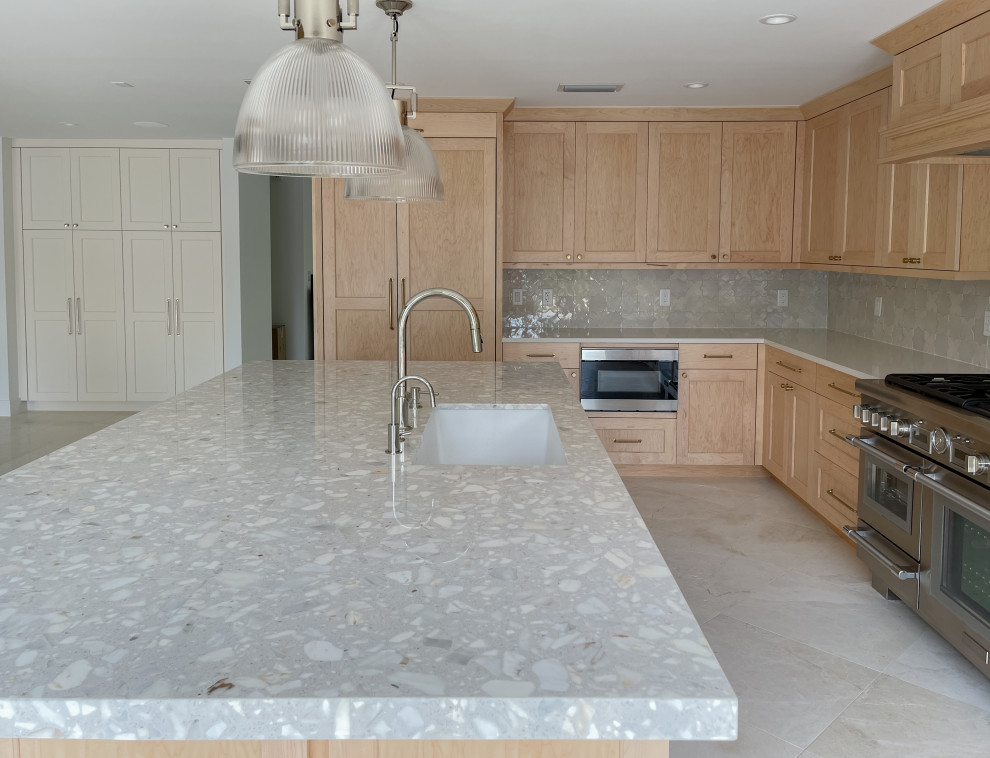 Photo of a mid-sized beach style l-shaped open plan kitchen in Miami with an undermount sink, shaker cabinets, light wood cabinets, marble benchtops, white splashback, terra-cotta splashback, stainless steel appliances, marble floors, with island, beige floor and grey benchtop.