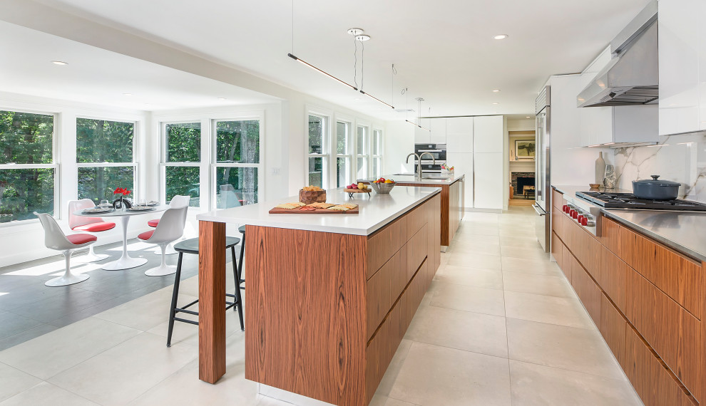 This is an example of a large contemporary eat-in kitchen in Boston with flat-panel cabinets, medium wood cabinets, stainless steel benchtops, white splashback, porcelain splashback, stainless steel appliances, porcelain floors, multiple islands and beige floor.