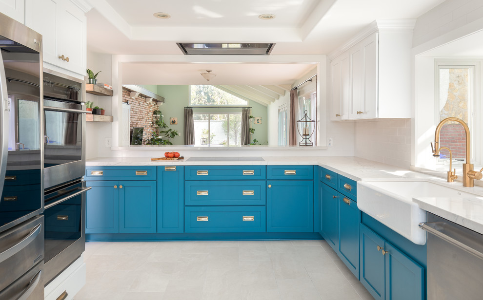 Photo of a transitional u-shaped kitchen in Los Angeles with a farmhouse sink, shaker cabinets, turquoise cabinets, stainless steel appliances, beige floor and beige benchtop.
