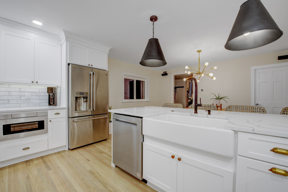 This is an example of a medium sized traditional u-shaped kitchen/diner in Philadelphia with a belfast sink, shaker cabinets, white cabinets, engineered stone countertops, white splashback, metro tiled splashback, light hardwood flooring, no island, beige floors and white worktops.