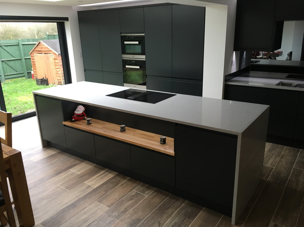 This is an example of a modern single-wall eat-in kitchen in Oxfordshire with an integrated sink, flat-panel cabinets, black cabinets, quartzite benchtops, mirror splashback, panelled appliances and with island.