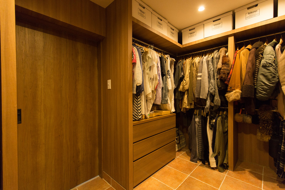 This is an example of a country gender-neutral dressing room in Osaka with terra-cotta floors, medium wood cabinets and orange floor.