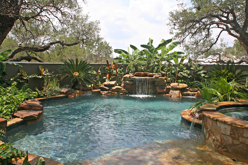 Photo of a mid-sized tropical backyard custom-shaped natural pool in Austin with natural stone pavers and a hot tub.