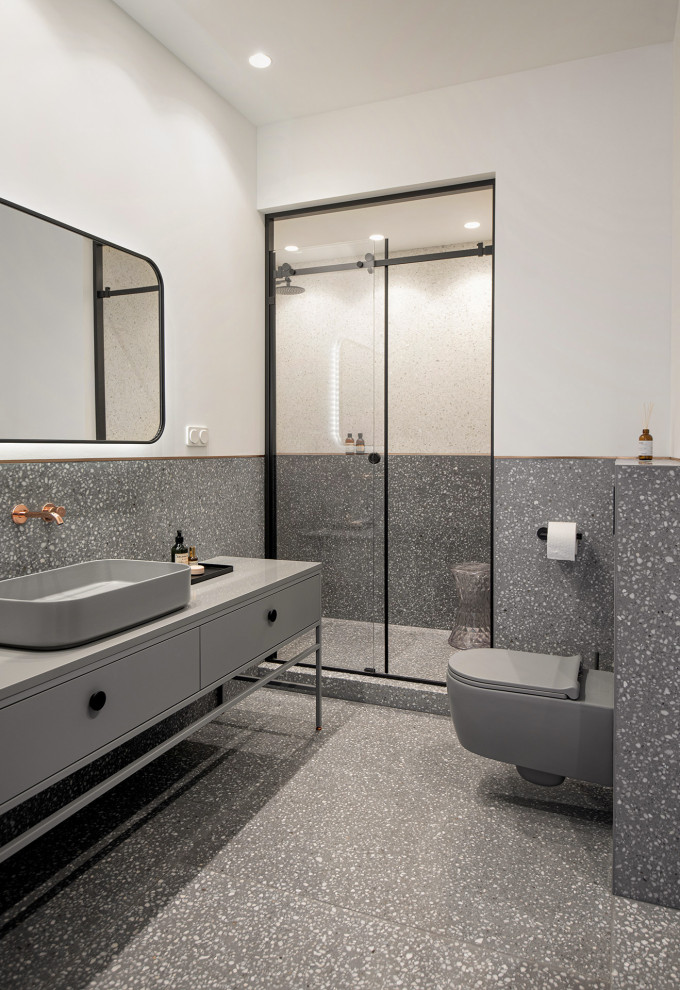 Стильный дизайн: серо-белая ванная комната среднего размера с плоскими фасадами, серыми фасадами, душем в нише, инсталляцией, серой плиткой, цементной плиткой, белыми стенами, полом из терраццо, душевой кабиной, накладной раковиной, столешницей из искусственного камня, серым полом, душем с раздвижными дверями, серой столешницей, тумбой под одну раковину и напольной тумбой - последний тренд