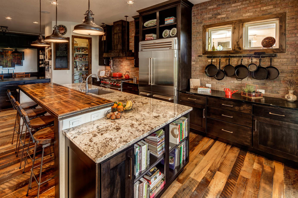 Large country l-shaped kitchen in Denver with an undermount sink, shaker cabinets, dark wood cabinets, red splashback, brick splashback, stainless steel appliances, medium hardwood floors, with island, brown floor and black benchtop.