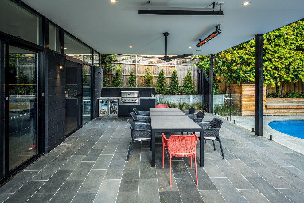 This is an example of a large backyard patio in Melbourne with an outdoor kitchen, natural stone pavers and an awning.