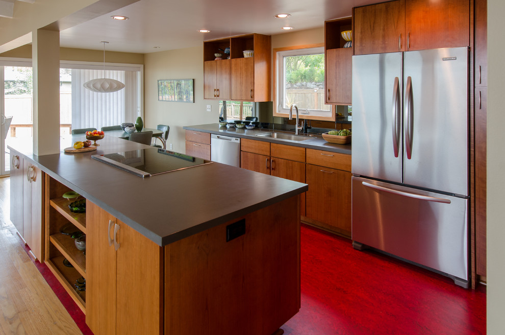 Photo of a mid-sized midcentury l-shaped kitchen in Seattle with flat-panel cabinets, medium wood cabinets, stainless steel appliances, mirror splashback, an undermount sink, with island, solid surface benchtops, linoleum floors and red floor.
