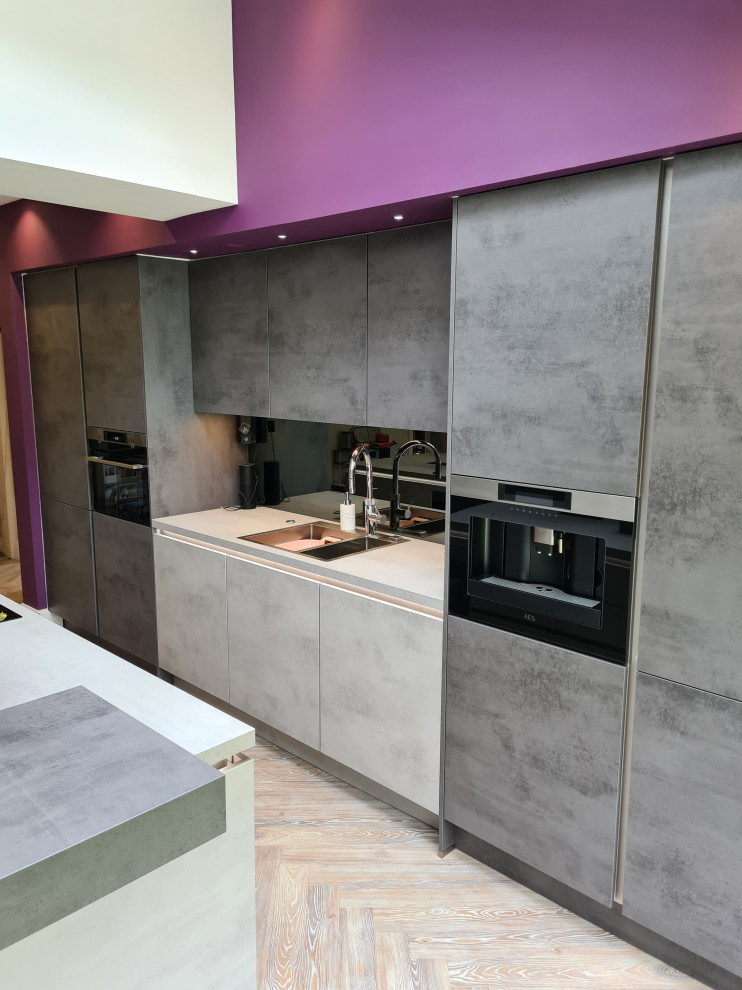 Inspiration for a large modern grey and purple single-wall kitchen/diner in Manchester with flat-panel cabinets, grey cabinets, composite countertops, metallic splashback, mirror splashback, black appliances, laminate floors, an island, brown floors, grey worktops and feature lighting.