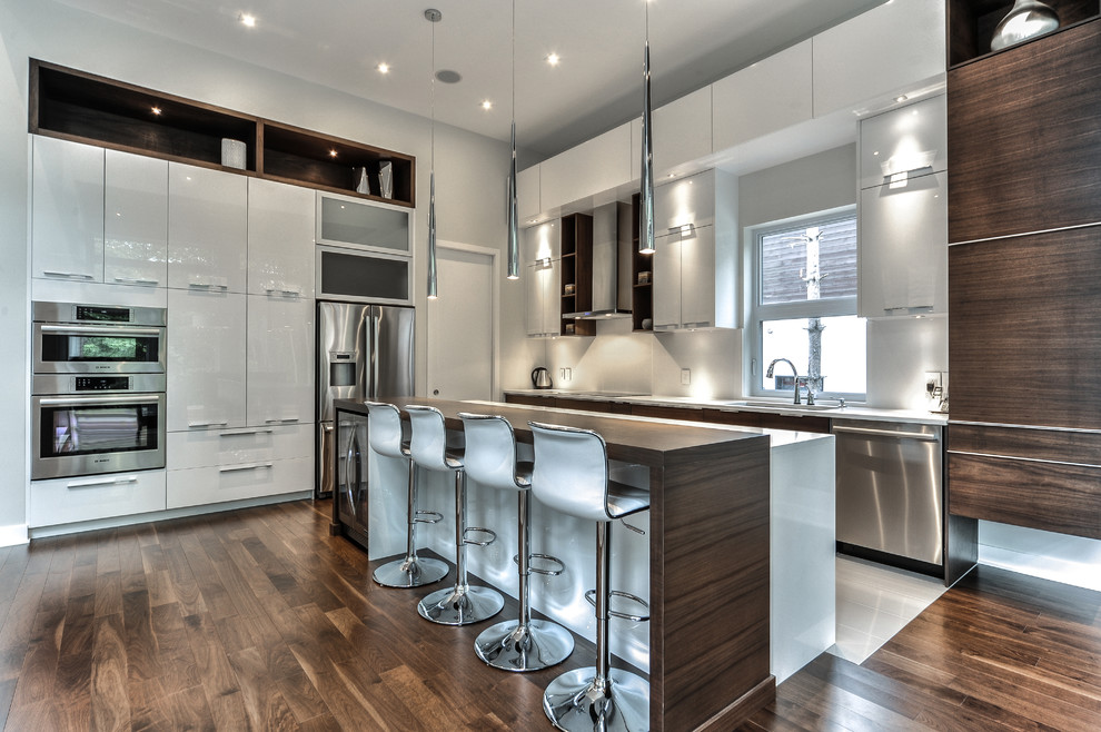 Inspiration for a large contemporary l-shaped kitchen in Montreal with an undermount sink, flat-panel cabinets, white cabinets, quartzite benchtops, white splashback, stone slab splashback, stainless steel appliances, medium hardwood floors and with island.