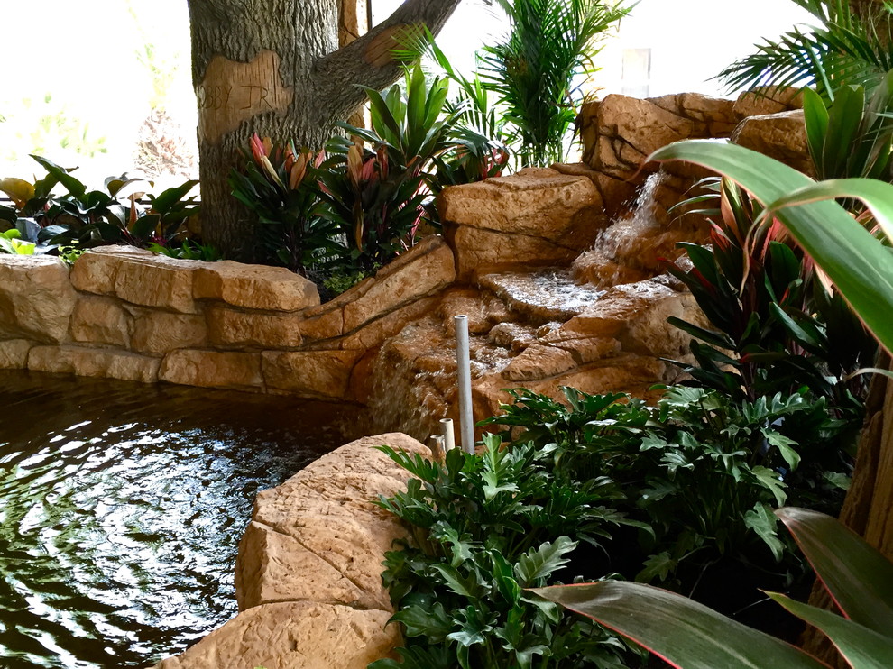 Inspiration for a mid-sized tropical backyard custom-shaped lap pool in Orlando with a water feature and natural stone pavers.