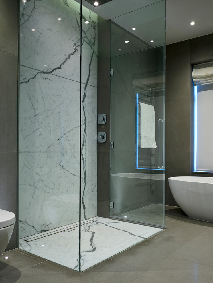 Design ideas for a mid-sized contemporary master bathroom in London with flat-panel cabinets, a freestanding tub, an open shower, a wall-mount toilet, beige walls, porcelain floors, a wall-mount sink and marble benchtops.