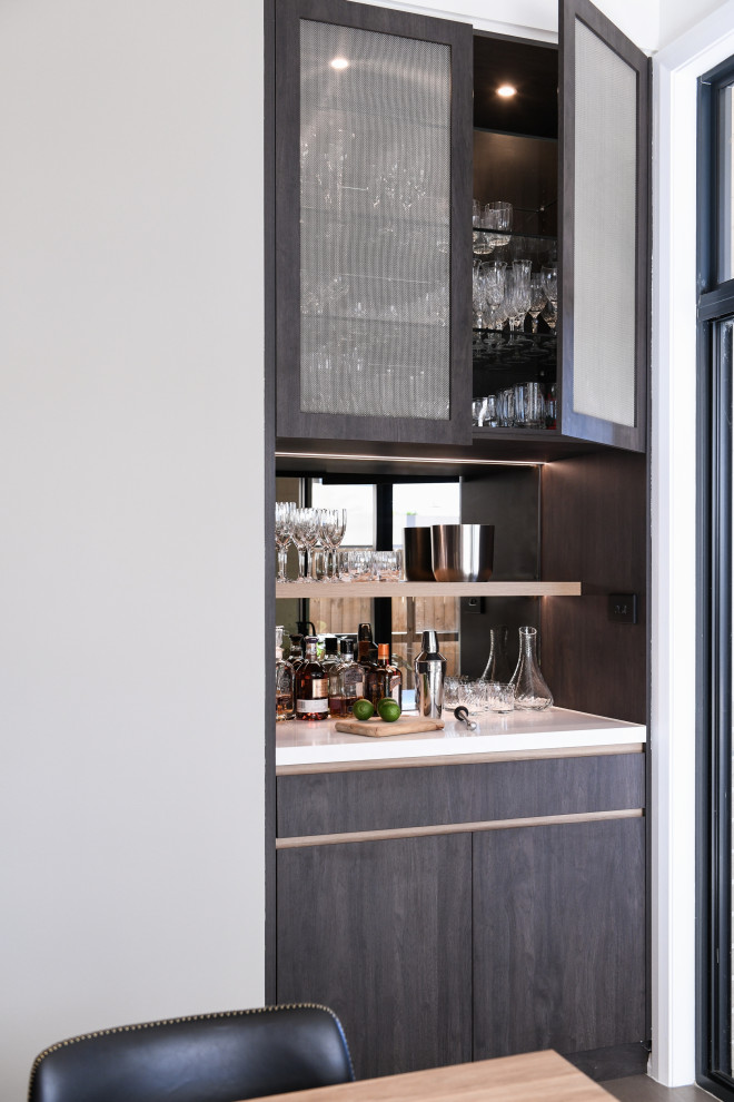 This is an example of a small contemporary single-wall home bar in Sydney with no sink, dark wood cabinets, quartz benchtops, multi-coloured splashback, mirror splashback, ceramic floors and white benchtop.