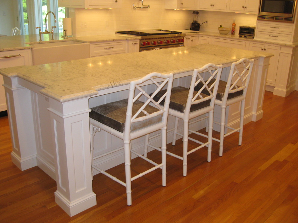 Example of a transitional u-shaped medium tone wood floor eat-in kitchen design in Boston with a farmhouse sink, beaded inset cabinets, white cabinets, marble countertops, white backsplash, subway tile backsplash, stainless steel appliances and an island