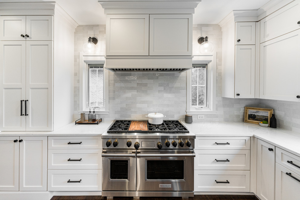 Large transitional l-shaped open plan kitchen in Chicago with an undermount sink, shaker cabinets, white cabinets, quartz benchtops, white splashback, ceramic splashback, stainless steel appliances, dark hardwood floors, with island, brown floor and white benchtop.