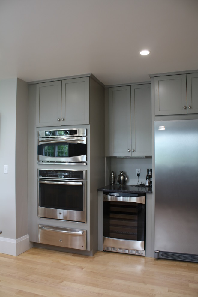 Inspiration for a modern l-shaped open plan kitchen in Boston with an undermount sink, shaker cabinets, grey cabinets, granite benchtops, grey splashback, stainless steel appliances, light hardwood floors and with island.