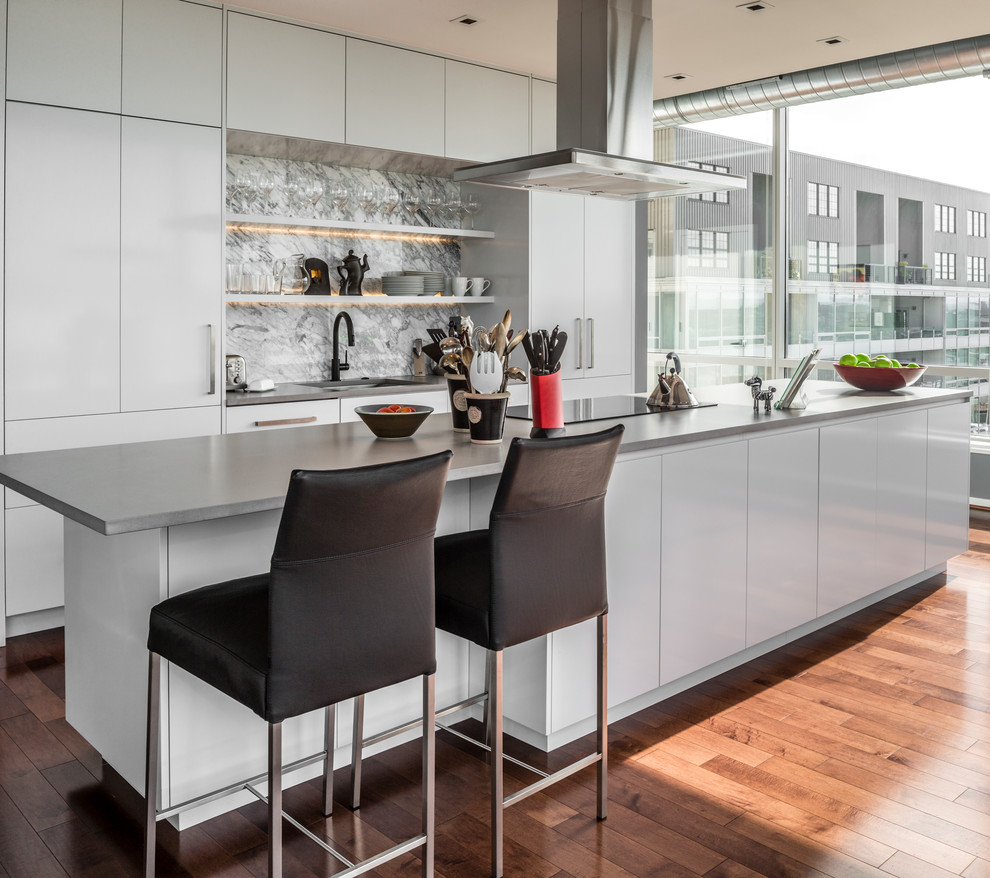 Huge trendy galley medium tone wood floor and brown floor open concept kitchen photo in Baltimore with an undermount sink, flat-panel cabinets, white cabinets, quartz countertops, gray backsplash, paneled appliances and an island