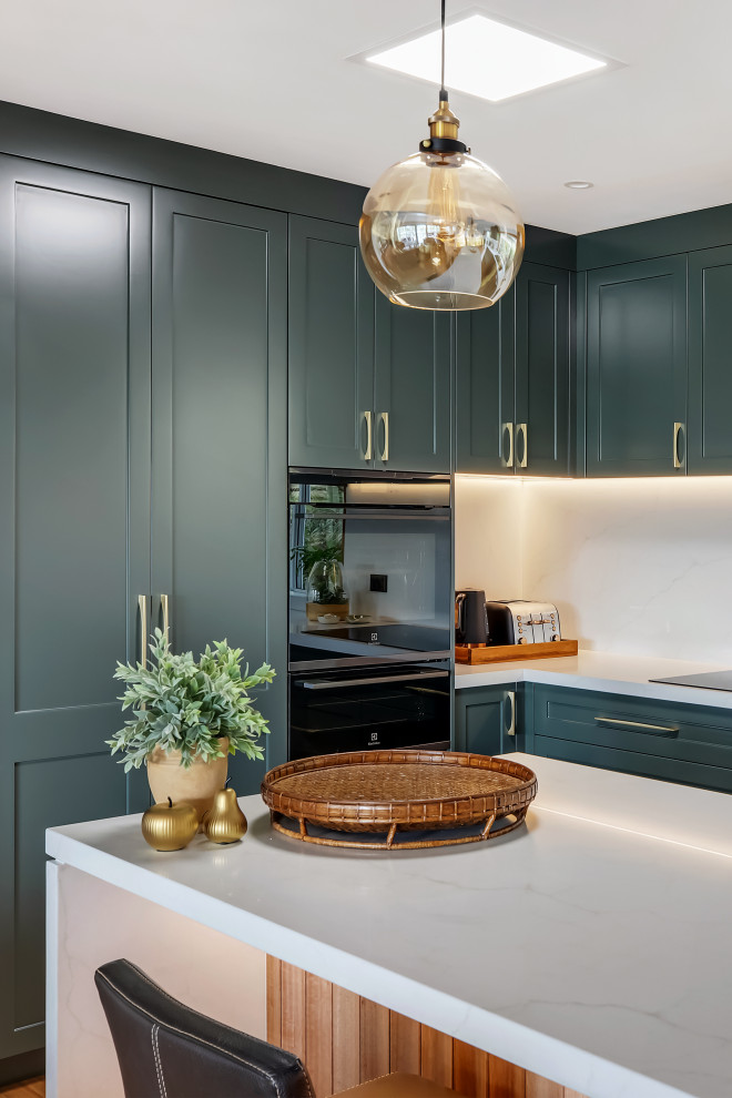 Large transitional l-shaped medium tone wood floor and multicolored floor eat-in kitchen photo in Sydney with a drop-in sink, shaker cabinets, green cabinets, quartz countertops, white backsplash, quartz backsplash, black appliances, an island and white countertops