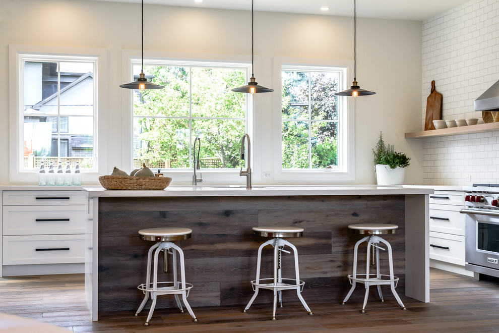 Large transitional l-shaped medium tone wood floor open concept kitchen photo in Toronto with a farmhouse sink, recessed-panel cabinets, white cabinets, white backsplash, subway tile backsplash, stainless steel appliances and an island