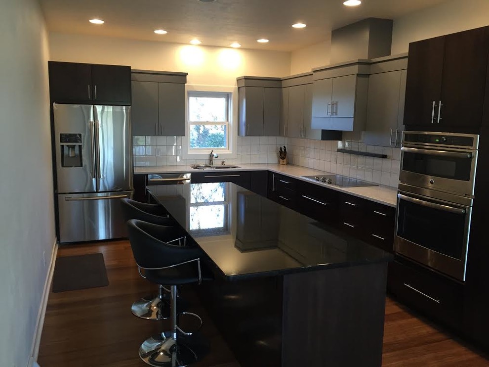 Eat-in kitchen - mid-sized transitional l-shaped medium tone wood floor eat-in kitchen idea in Cedar Rapids with a double-bowl sink, flat-panel cabinets, gray cabinets, quartz countertops, white backsplash, ceramic backsplash, stainless steel appliances and an island