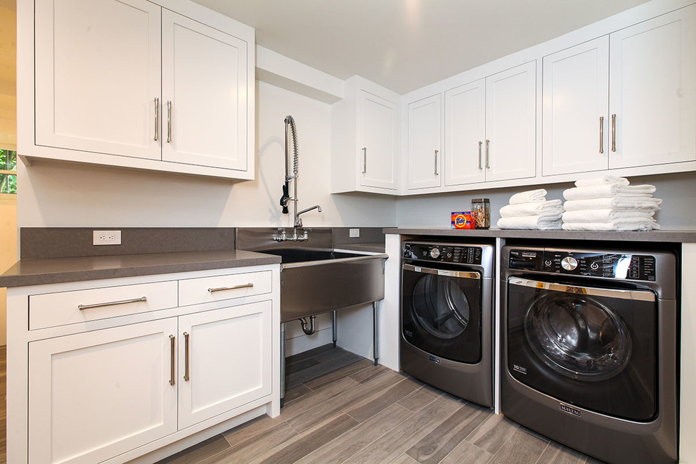 Design ideas for an expansive transitional l-shaped dedicated laundry room in San Francisco with recessed-panel cabinets, white cabinets, quartz benchtops, white walls, porcelain floors, a side-by-side washer and dryer, an utility sink, beige floor and grey benchtop.