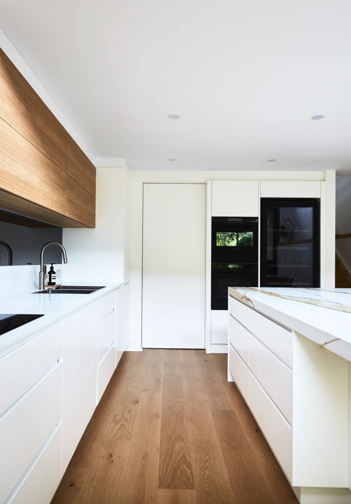 Photo of a large contemporary l-shaped kitchen pantry in Sydney with a double-bowl sink, flat-panel cabinets, white cabinets, quartz benchtops, multi-coloured splashback, mirror splashback, black appliances, laminate floors, with island and multi-coloured benchtop.