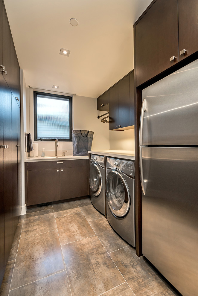 This is an example of a large modern galley dedicated laundry room in San Diego with an undermount sink, flat-panel cabinets, dark wood cabinets, quartz benchtops, grey walls, porcelain floors and a side-by-side washer and dryer.