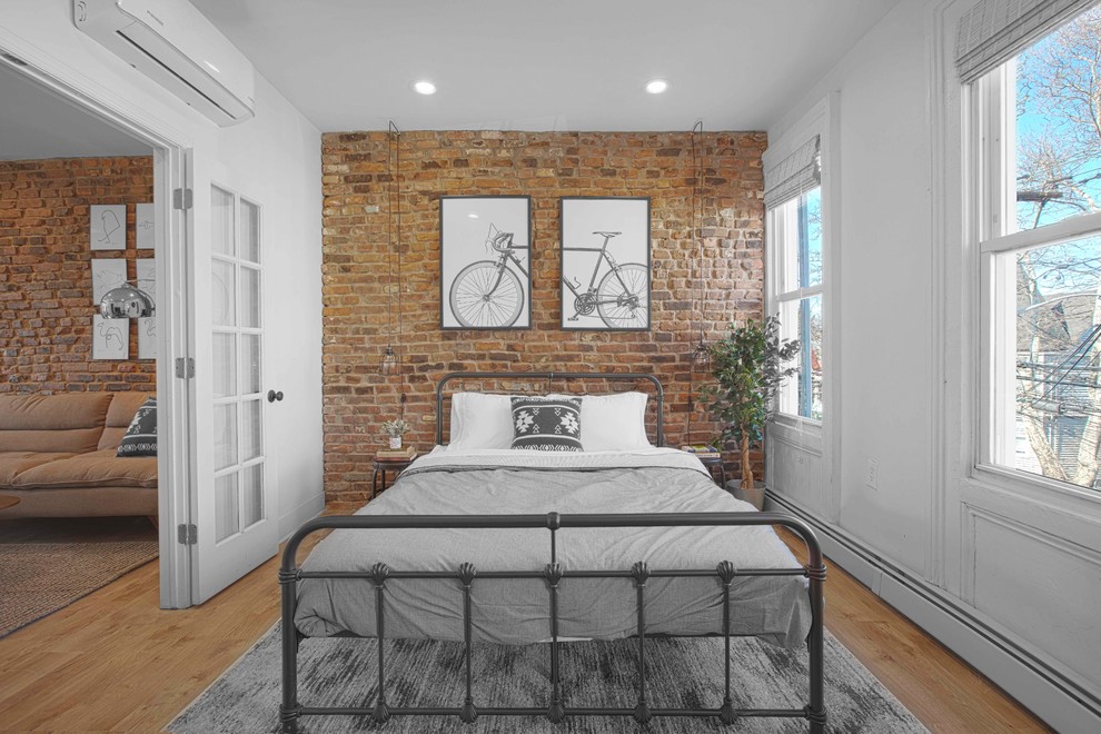 This is an example of an industrial bedroom in New York with white walls, medium hardwood floors and no fireplace.