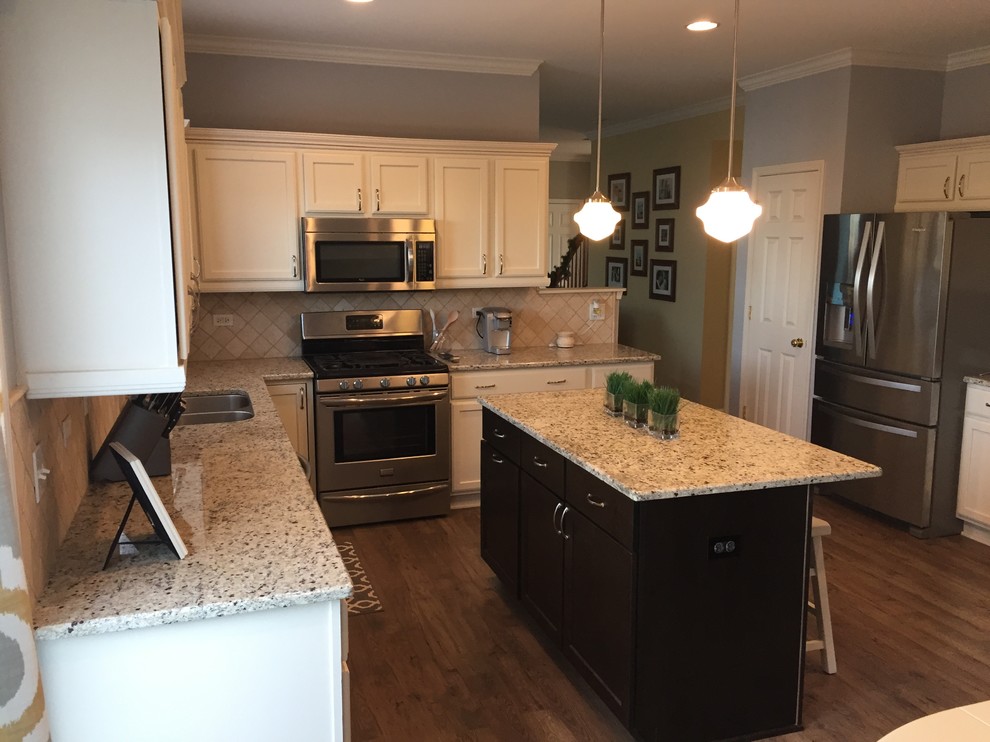 Example of a mid-sized transitional laminate floor kitchen design in Chicago with an undermount sink, recessed-panel cabinets, granite countertops, beige backsplash, stone tile backsplash, stainless steel appliances and an island