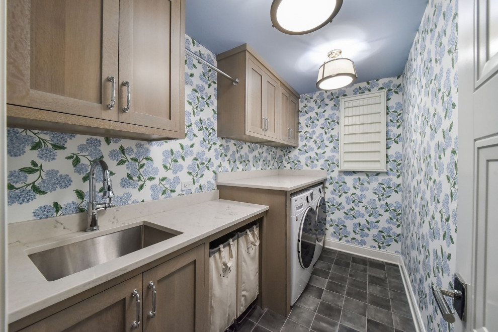 This is an example of a mid-sized galley dedicated laundry room in Chicago with an undermount sink, shaker cabinets, beige cabinets, multi-coloured walls, a side-by-side washer and dryer, grey floor, beige benchtop and wallpaper.