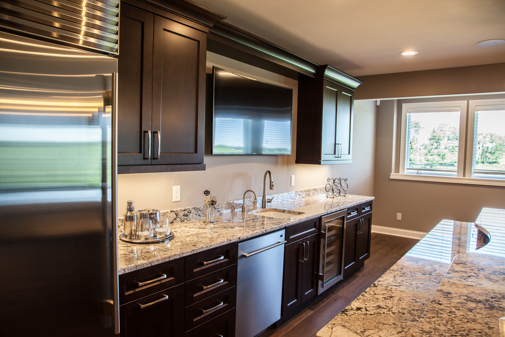 Photo of a transitional l-shaped home bar in Other with shaker cabinets, dark wood cabinets, granite benchtops, beige splashback, glass tile splashback, dark hardwood floors, brown floor and brown benchtop.