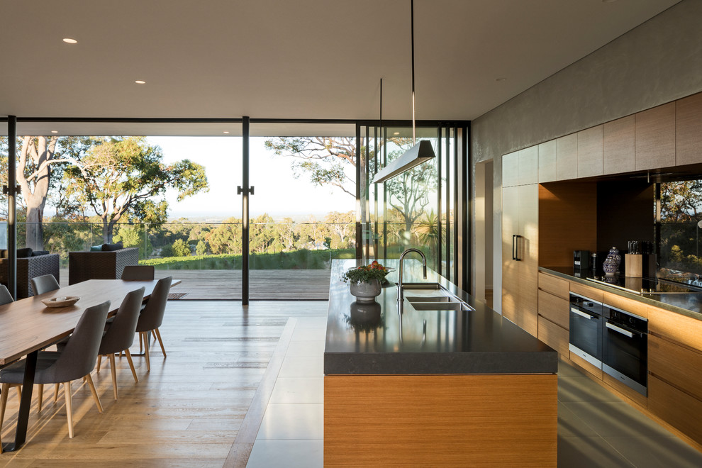 Design ideas for a large contemporary single-wall kitchen in Perth with a triple-bowl sink, recessed-panel cabinets, light wood cabinets, marble benchtops, black splashback, glass tile splashback, stainless steel appliances, porcelain floors, with island, grey floor and grey benchtop.