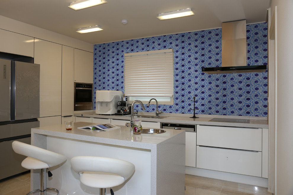 Large modern galley eat-in kitchen in Gold Coast - Tweed with white cabinets, blue splashback, with island, a double-bowl sink, louvered cabinets, solid surface benchtops, stainless steel appliances, porcelain floors, beige floor, beige benchtop and glass tile splashback.